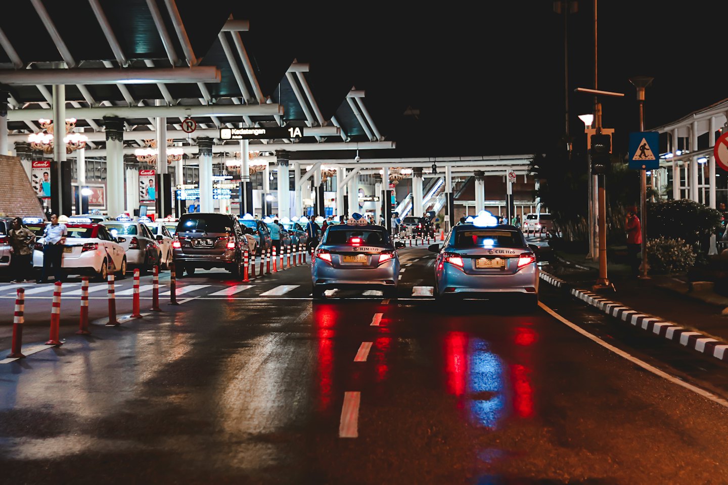 Taxis en auto's die wachten op passagiers onder een groot terminaldak.